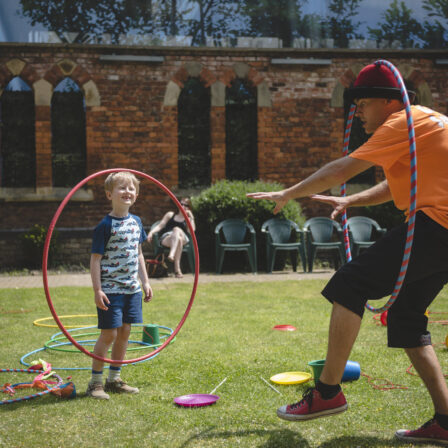 A hula hoop artist performs in front of a smiling child.