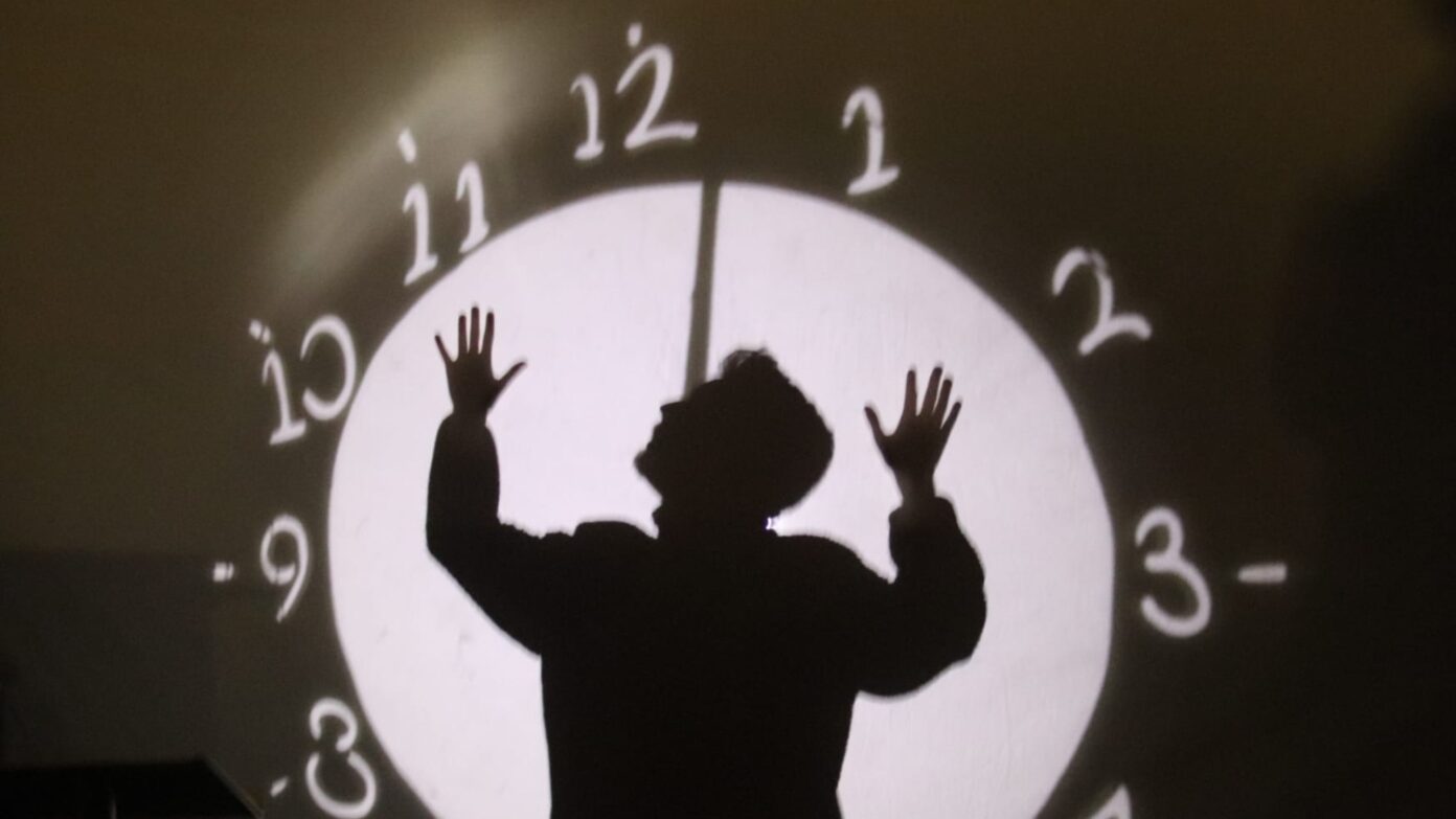 Performer's shadow on a large clock backdrop.