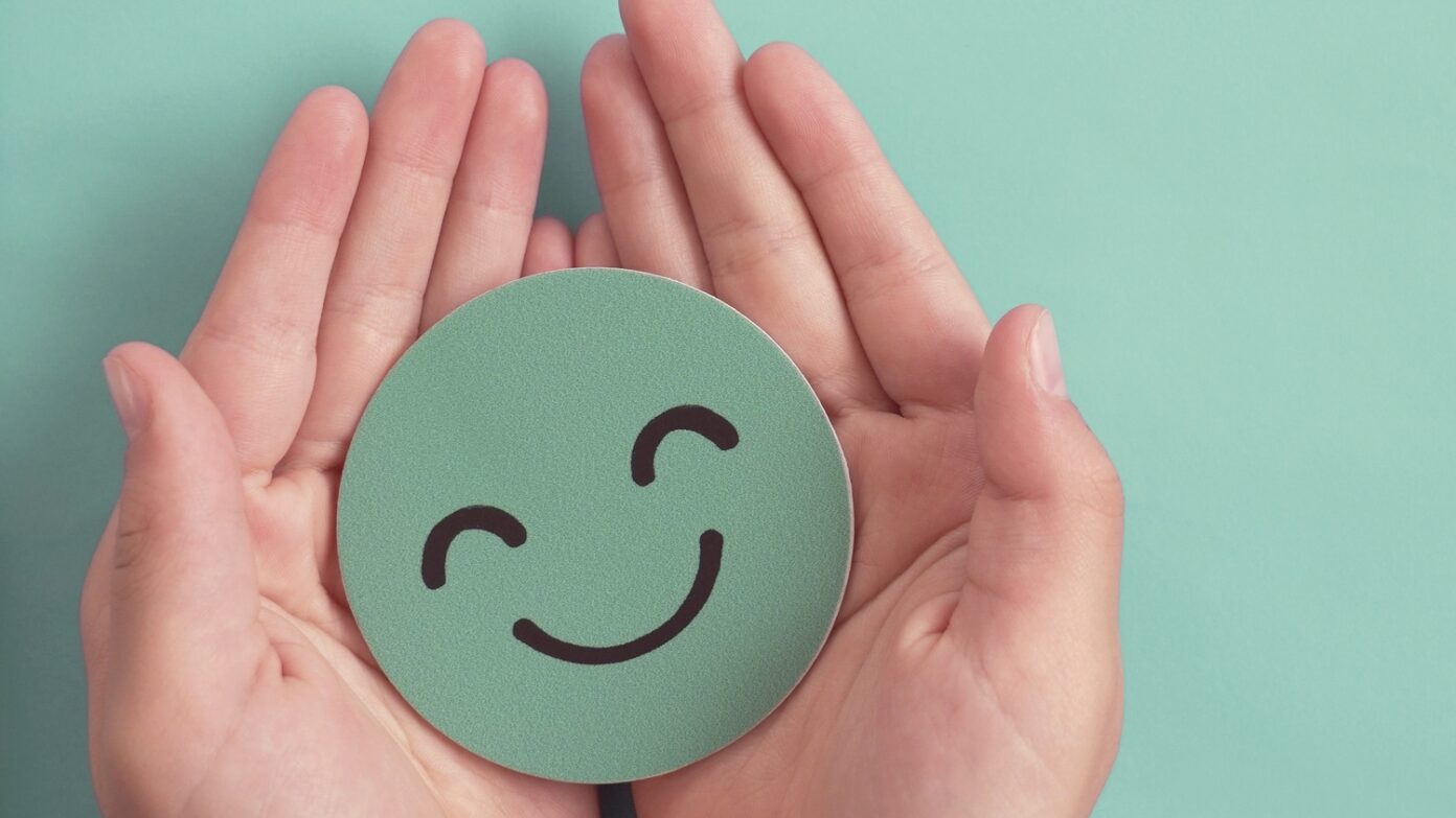 Hands holding green happy smile face paper cut.