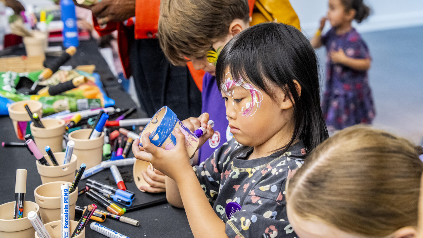 Young person with face painted deocrating a plant pot
