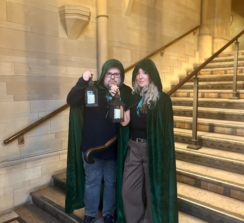 Two people dressed in capes carrying lanterns on a staircase
