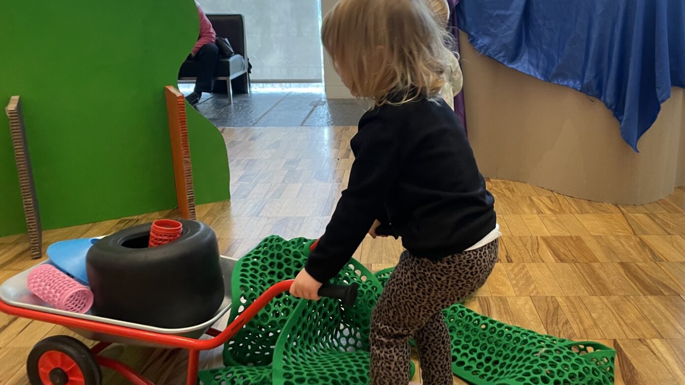 Small child moving mat and wheelbarrow in gallery